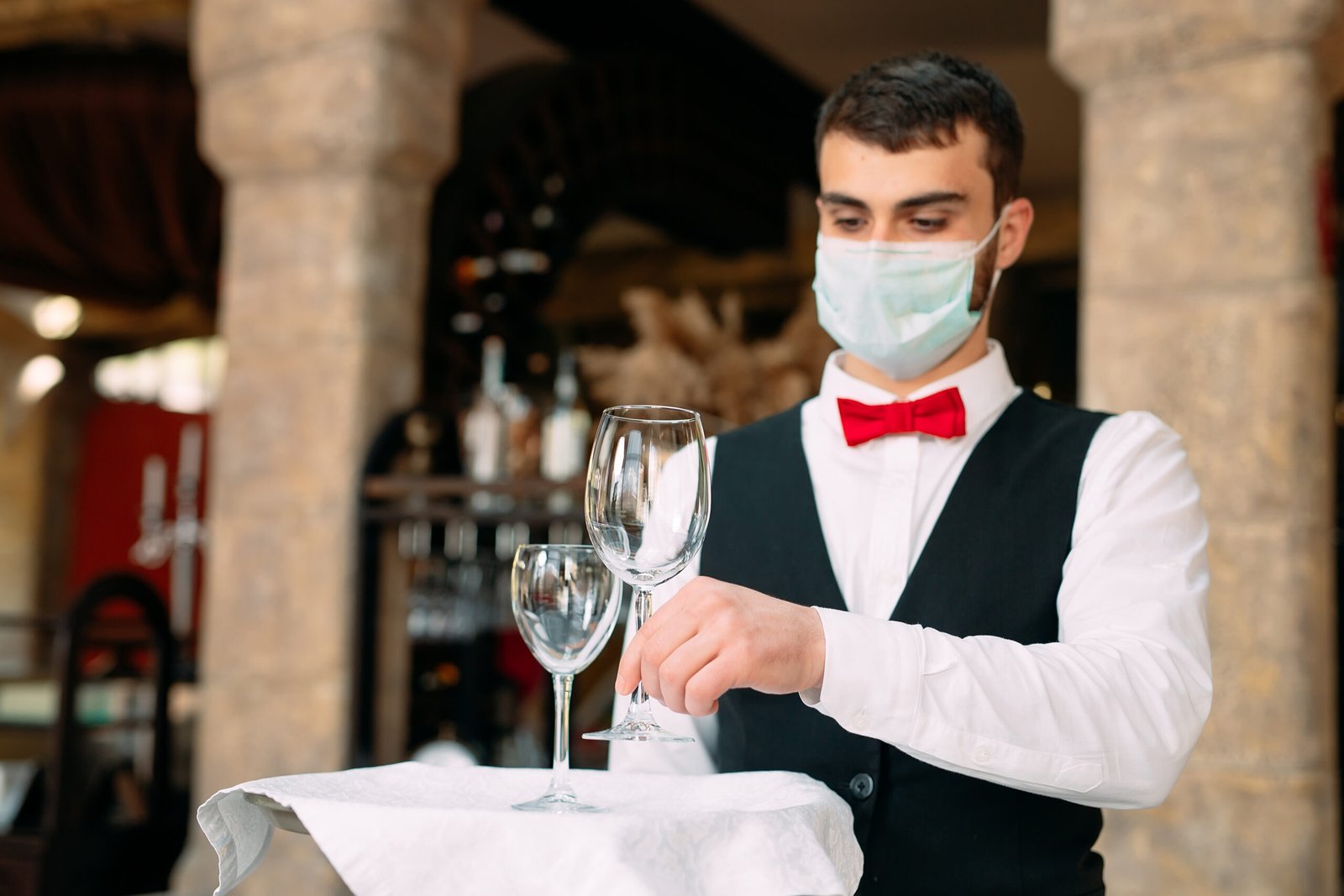 Waiter wearing mask and serving wine glasses – hospitality job opportunity in UK